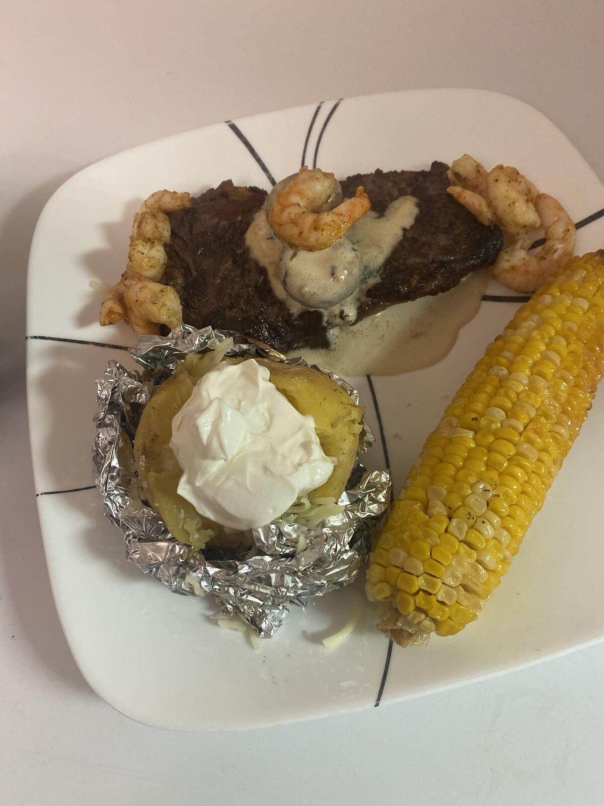 Steak and shrimp with a loaded baked potato and corn